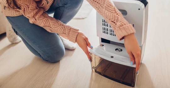 Woman changing water container of dehumidifier at home