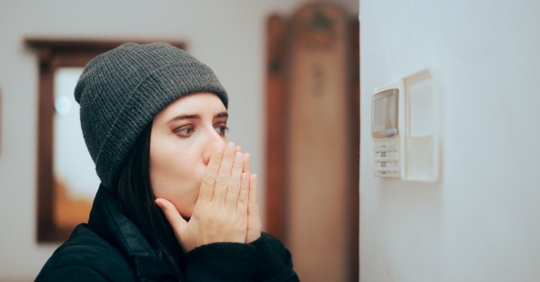 Woman staring at a thermostat while feeling cold