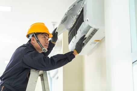 An electrician services an air conditioner